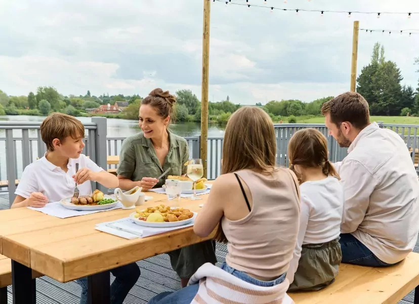 Family enjoying a meal together at an outdoor lakeside restaurant terrace with scenic views at Billing Aquadrome.