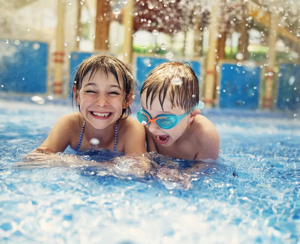 Two smiling children having fun splashing and swimming in the indoor pool during a family holiday at Billing Aquadrome.