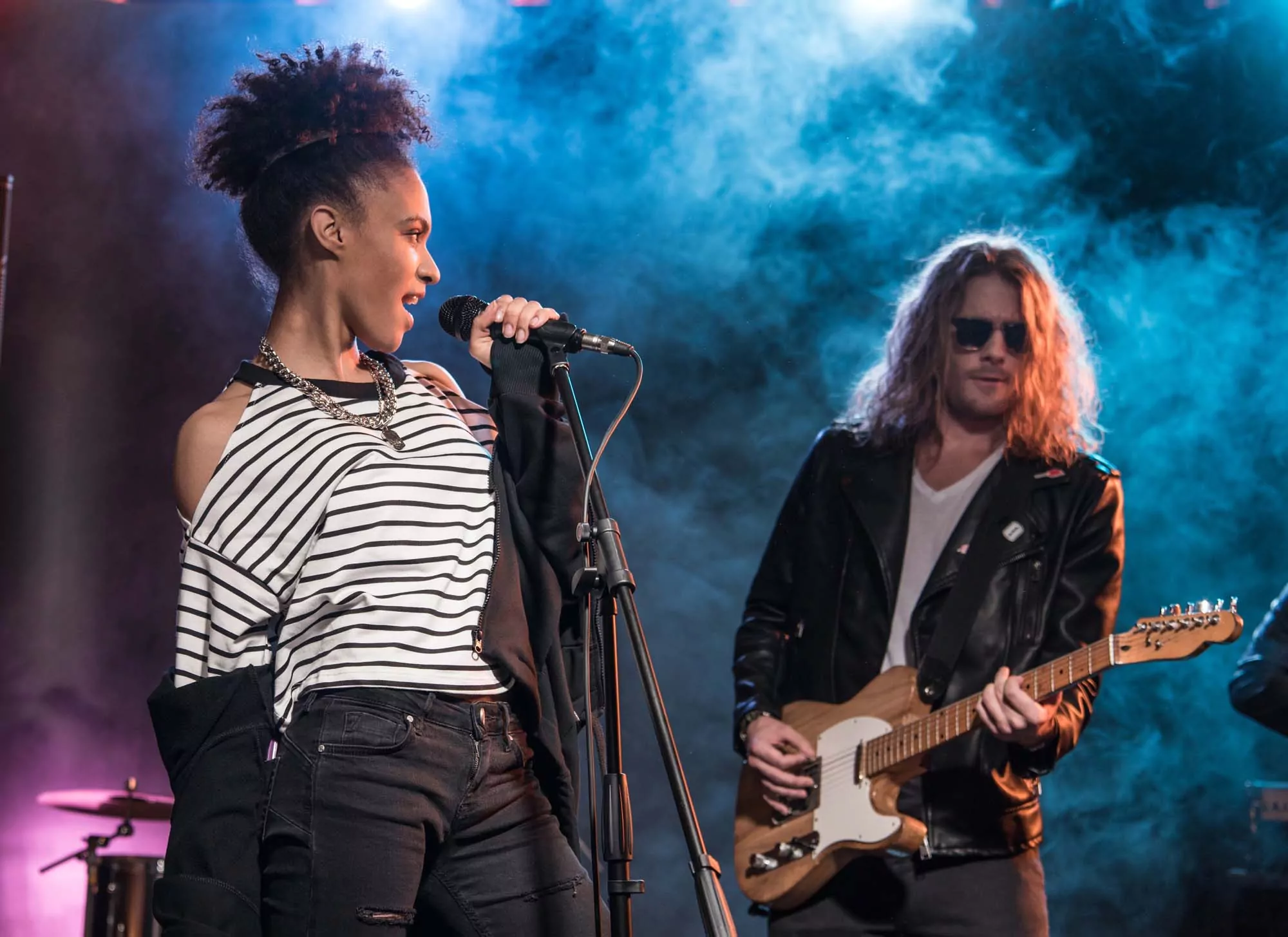 Female singer with microphone and rock and roll band performing hard rock music on stage