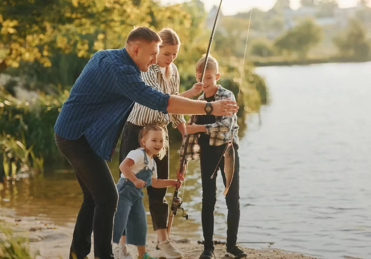 A family fishing together by the lakeside at Billing Aquadrome, smiling as they catch a fish.