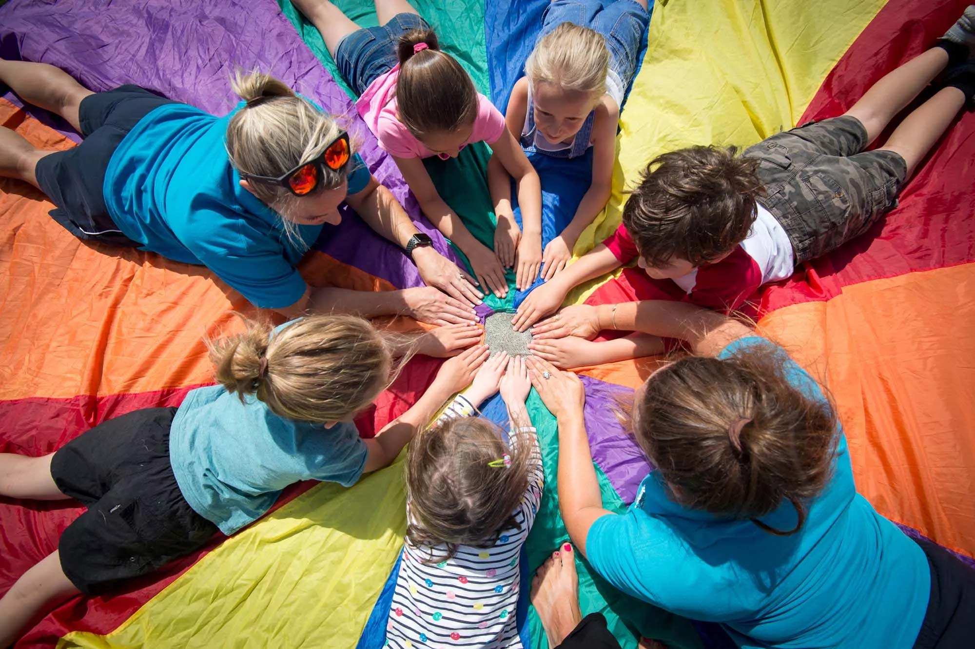 Children and adults at Billing Aquadrome playing a colourful parachute game outdoors.