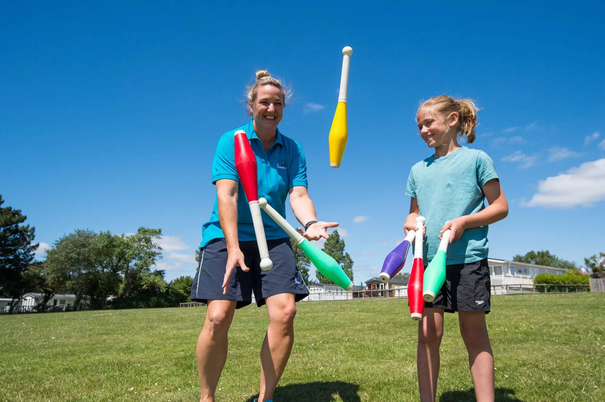 Instructor teaching a child how to juggle colourful clubs outdoors at Billing Aquadrome
