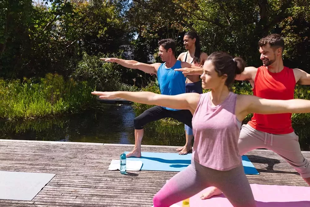 Group of people practicing yoga poses outdoors by the water at Billing Aquadrome