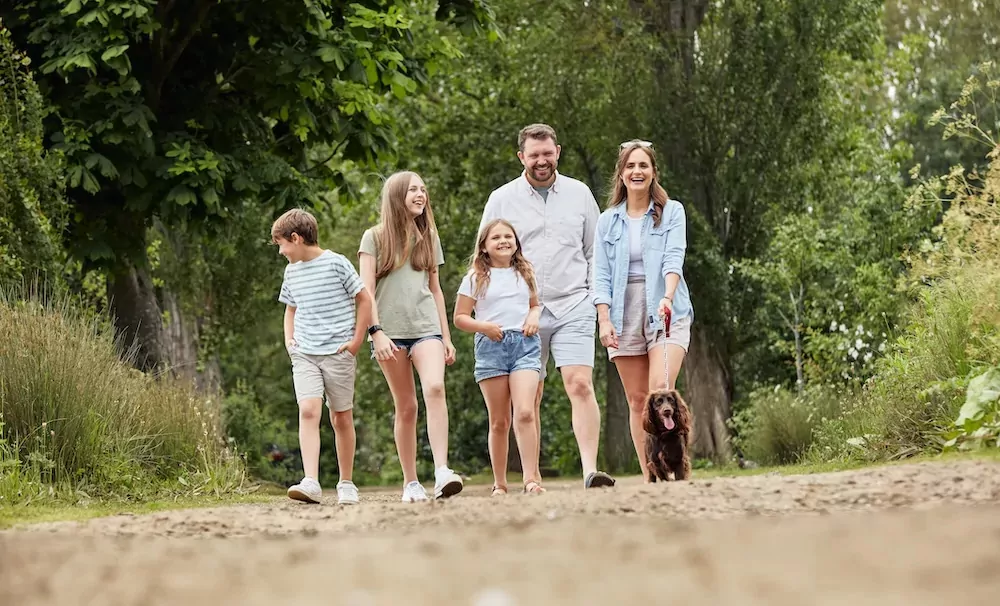 Happy family walking their dog along a scenic woodland path at Billing Aquadrome