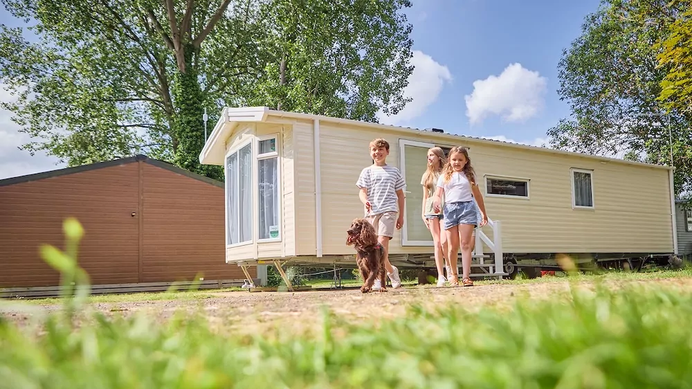 UK dog friendly holidays at Billing Aquadrome - image showing family walking their dog outside their caravan