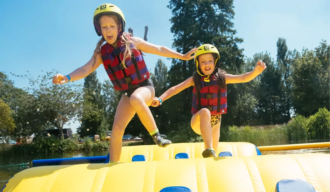 Two young girls enjoying a water obstacle course on an inflatable raft, laughing and splashing in the fun-filled adventure.