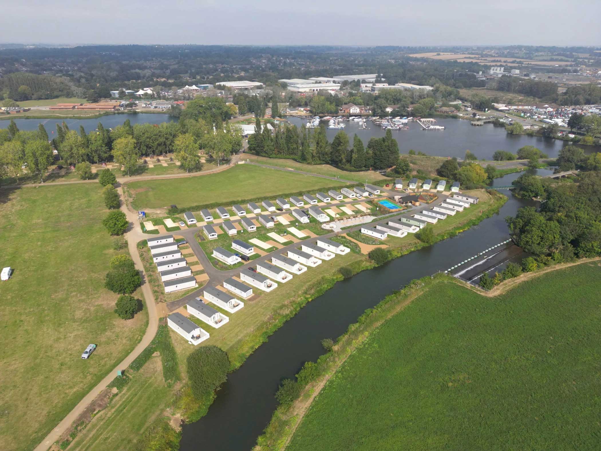 Aerial view of the caravan park at Billing Aquadrome, showing rows of holiday homes, surrounding green fields, and a river running alongside the site