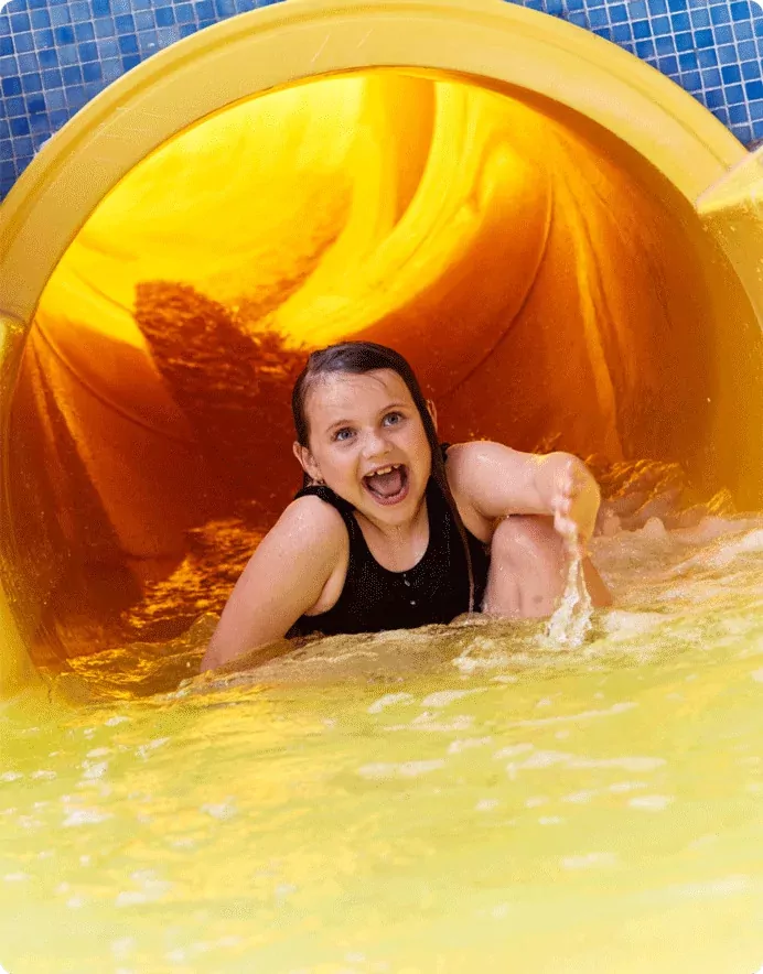 Smiling child splashing into the pool from a yellow water slide at Billing Aquadrome.