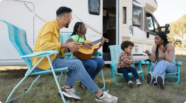 A young family playing with a guitar outside their Campervan
