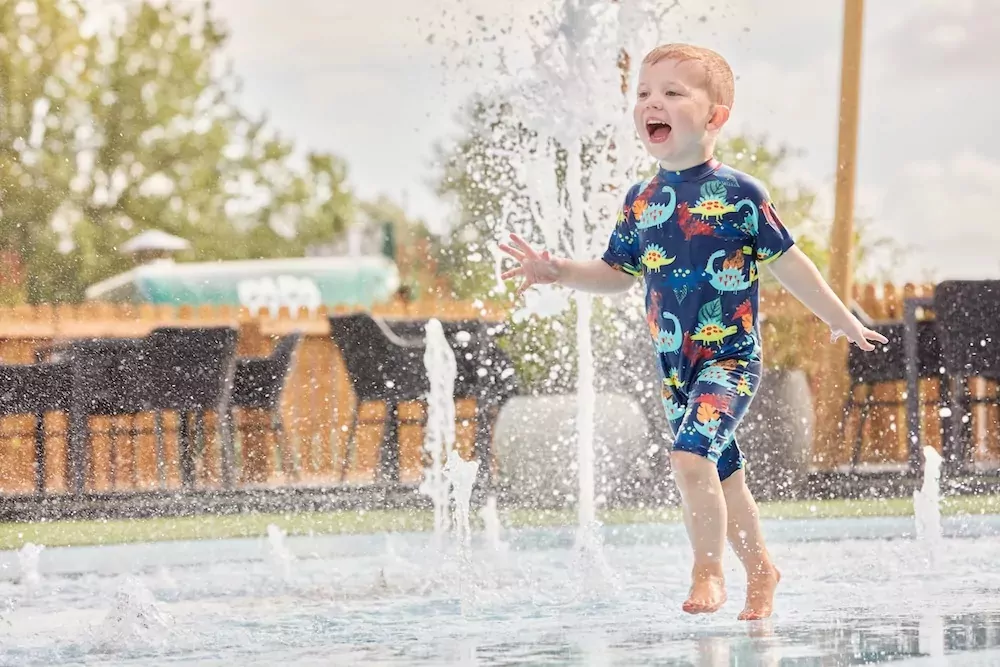Young boy laughing and playing in the splash park fountains at Billing Aquadrome on a sunny day