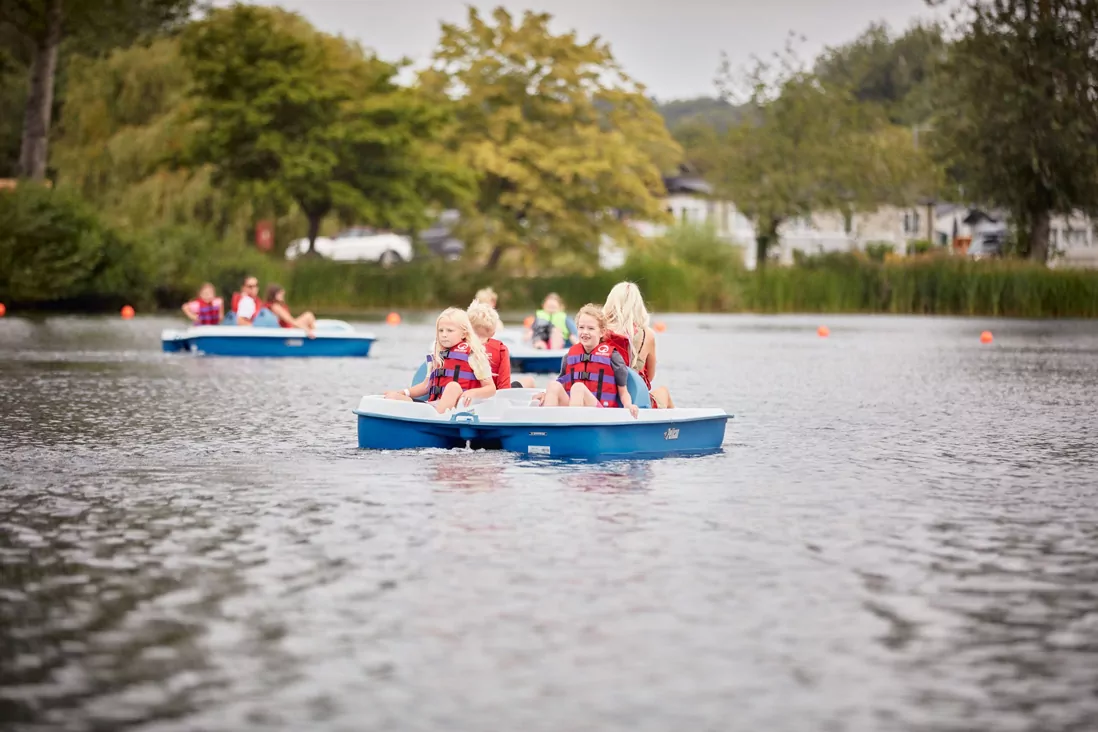Children riding pedal boats on a peaceful lake surrounded by greenery.
