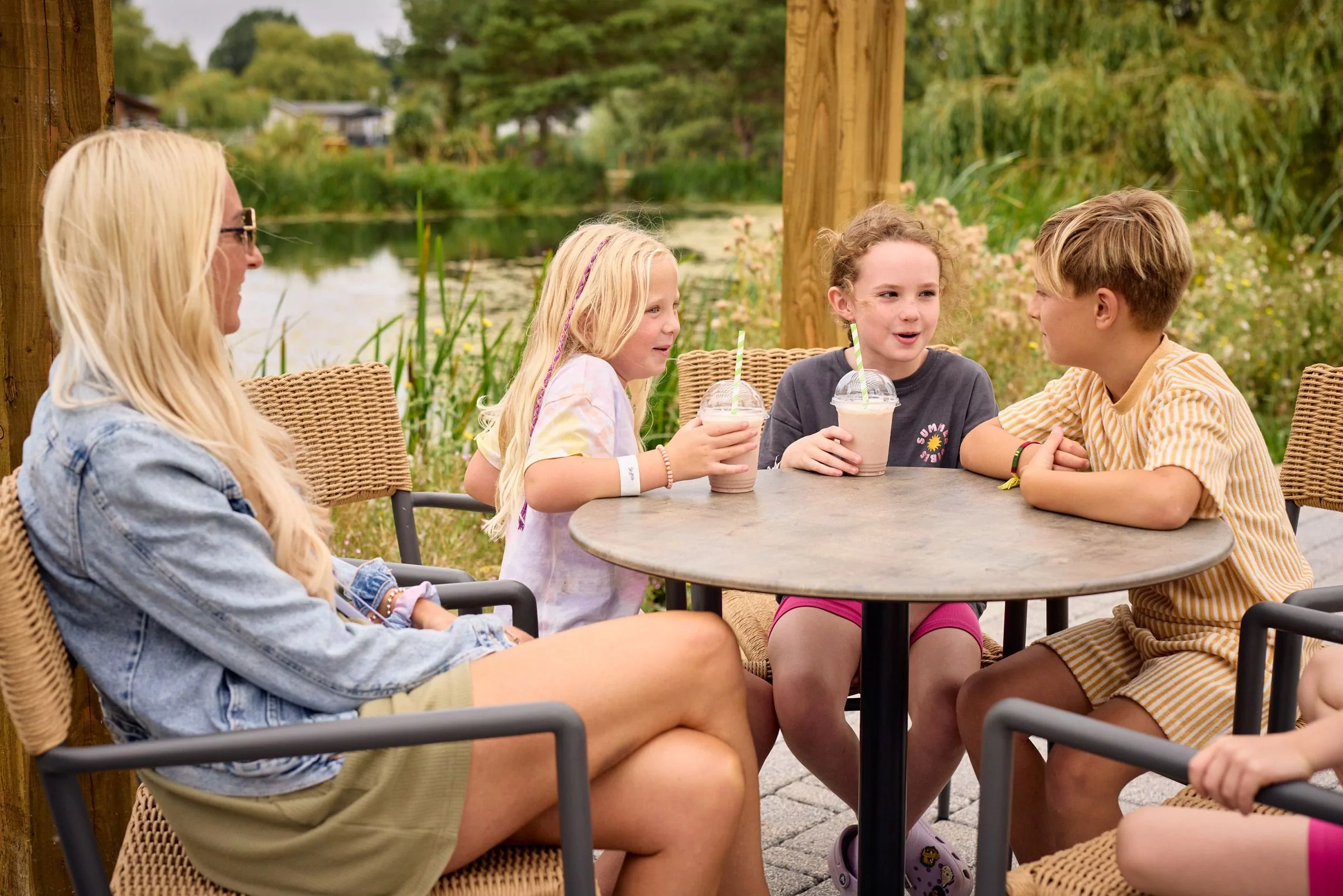 Family enjoying milkshakes together at an outdoor seating area beside a scenic lake.