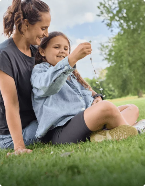 A child and their mother making a daisy chain on the grass