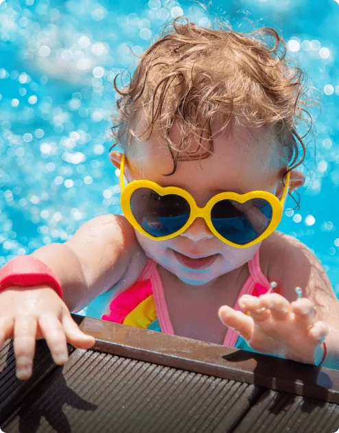 A young child wearing yellow love heart sunglasses sat in a pool