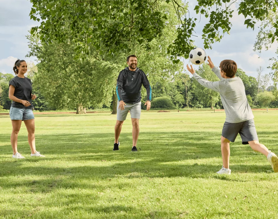 A group of 3 people playing catch with a football under a tree