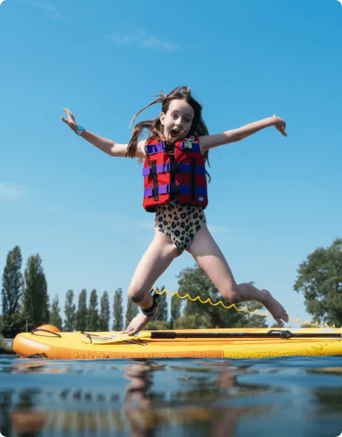 A young girl is energetically jumping on a paddleboard, capturing a moment of fun and adventure on the water.