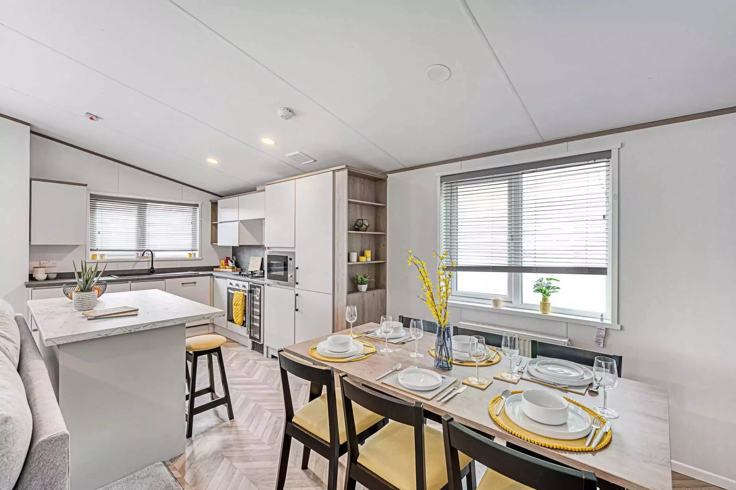 Full view of a bright and modern static caravan kitchen and dining area at Meadow Bay Villages, featuring a set table and island breakfast bar.