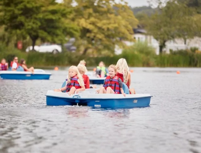 Group of children wearing life jackets and pedalling together on a boat at Meadow Bay Villages’ scenic lake.