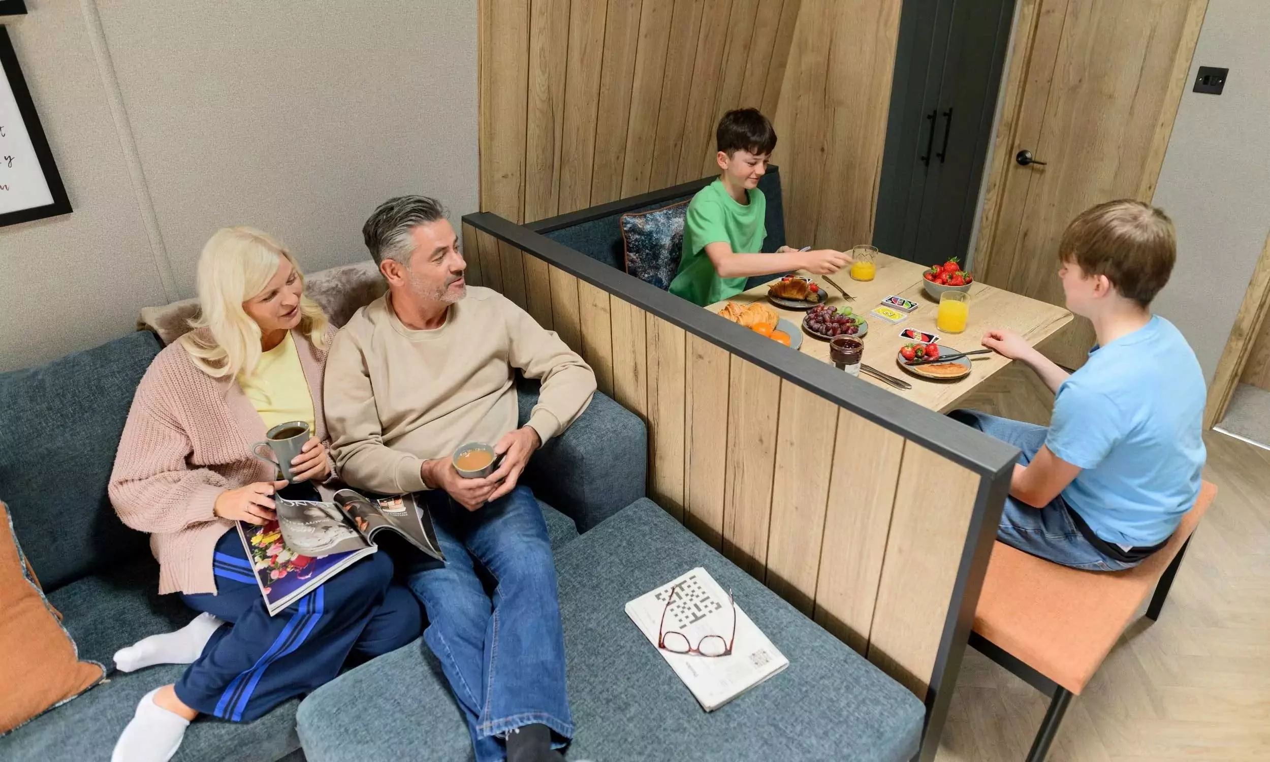 Family relaxing inside a modern holiday lodge with a cosy lounge and breakfast area at Billing Aquadrome, Meadow Bay Villages.
