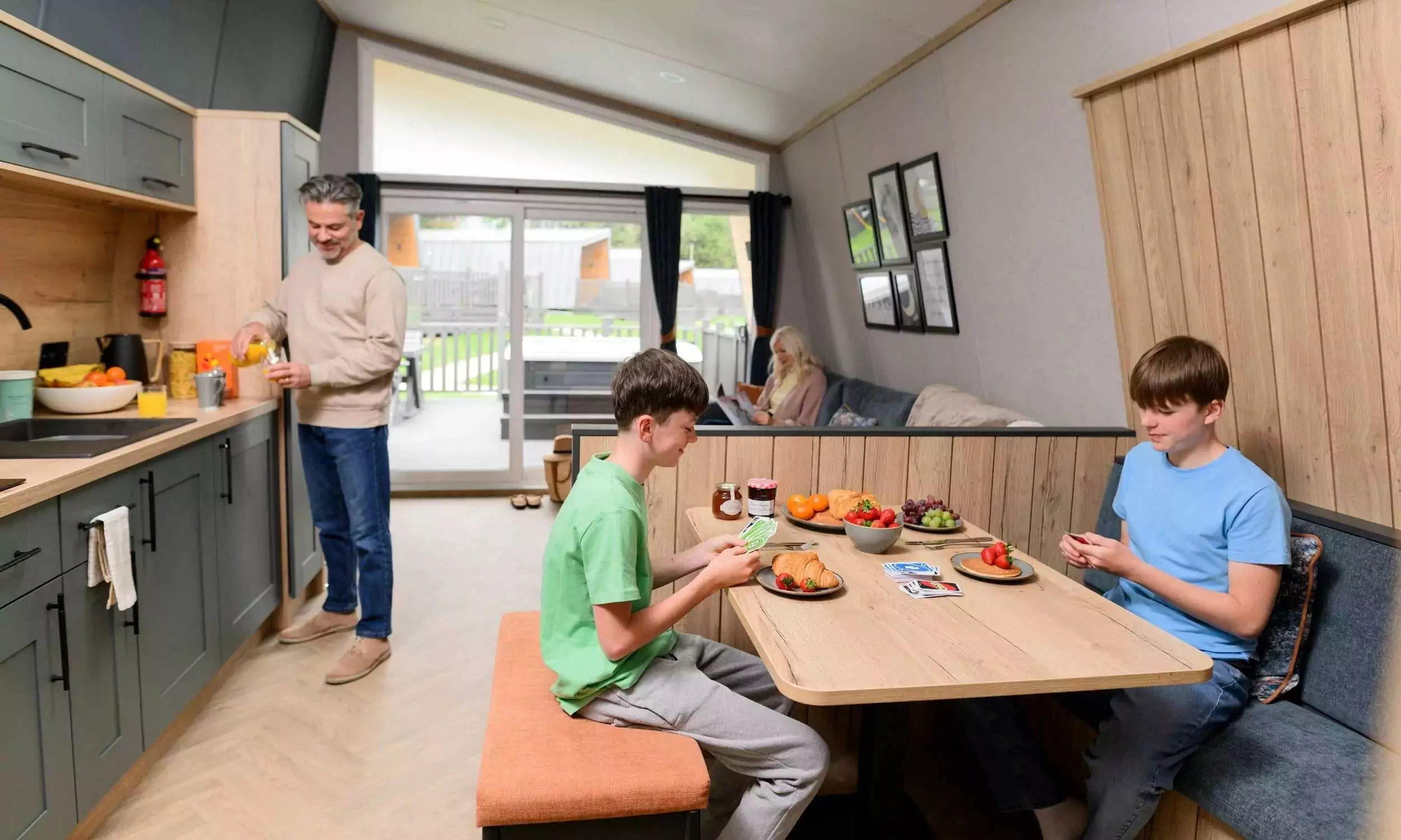 Family spending time together in a modern open-plan holiday lodge at Billing Aquadrome, part of Meadow Bay Villages — with kitchen, dining area and lounge.