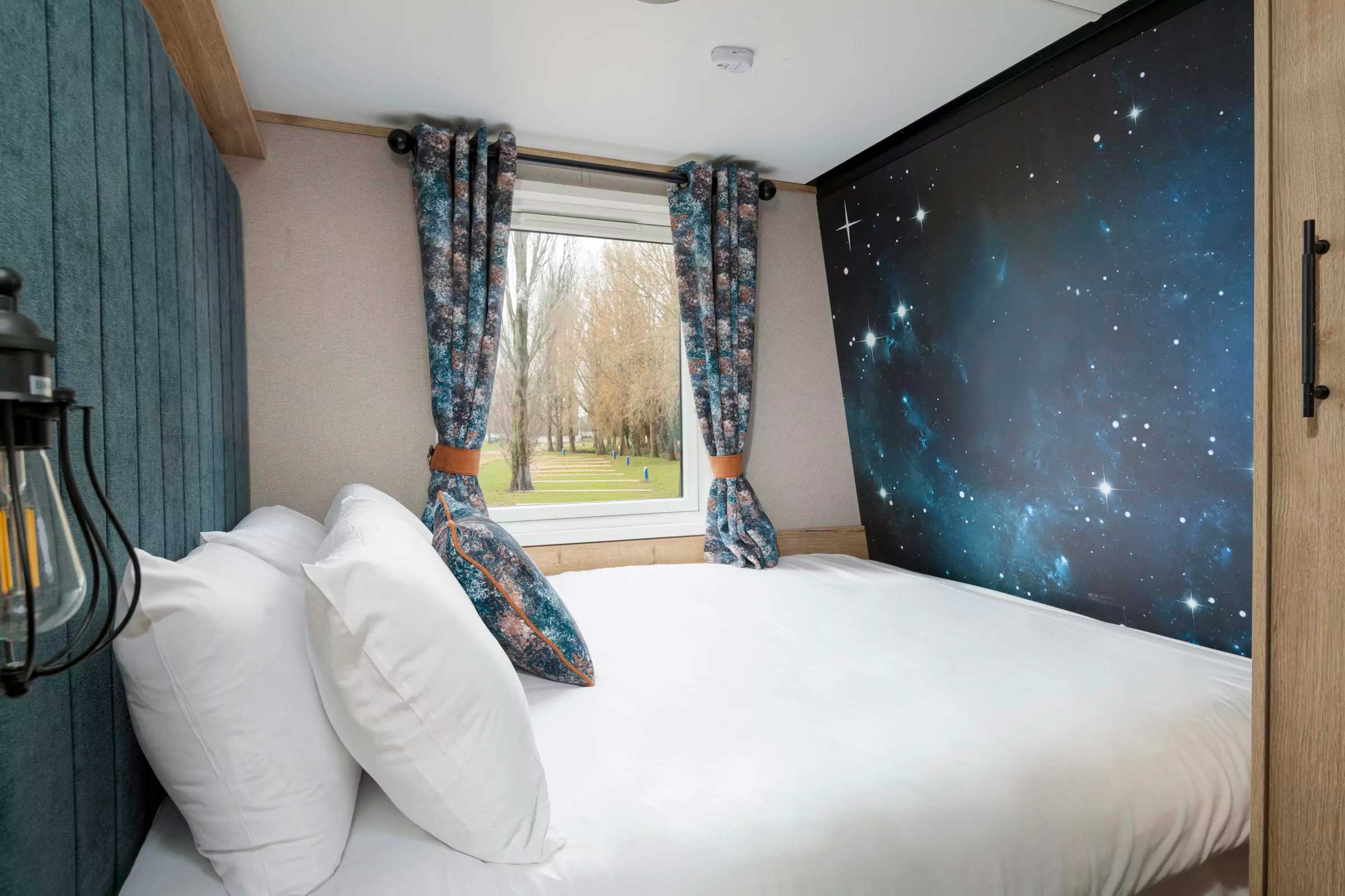 Comfortable double bedroom in a holiday lodge with space-themed feature wall and scenic park views at Billing Aquadrome, Meadow Bay Villages.