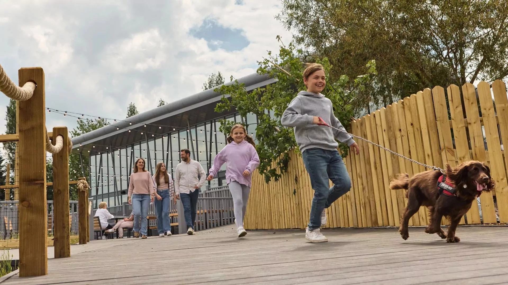Children running with a dog on a lead along a wooden boardwalk, with family walking behind at Meadow Bay Villages