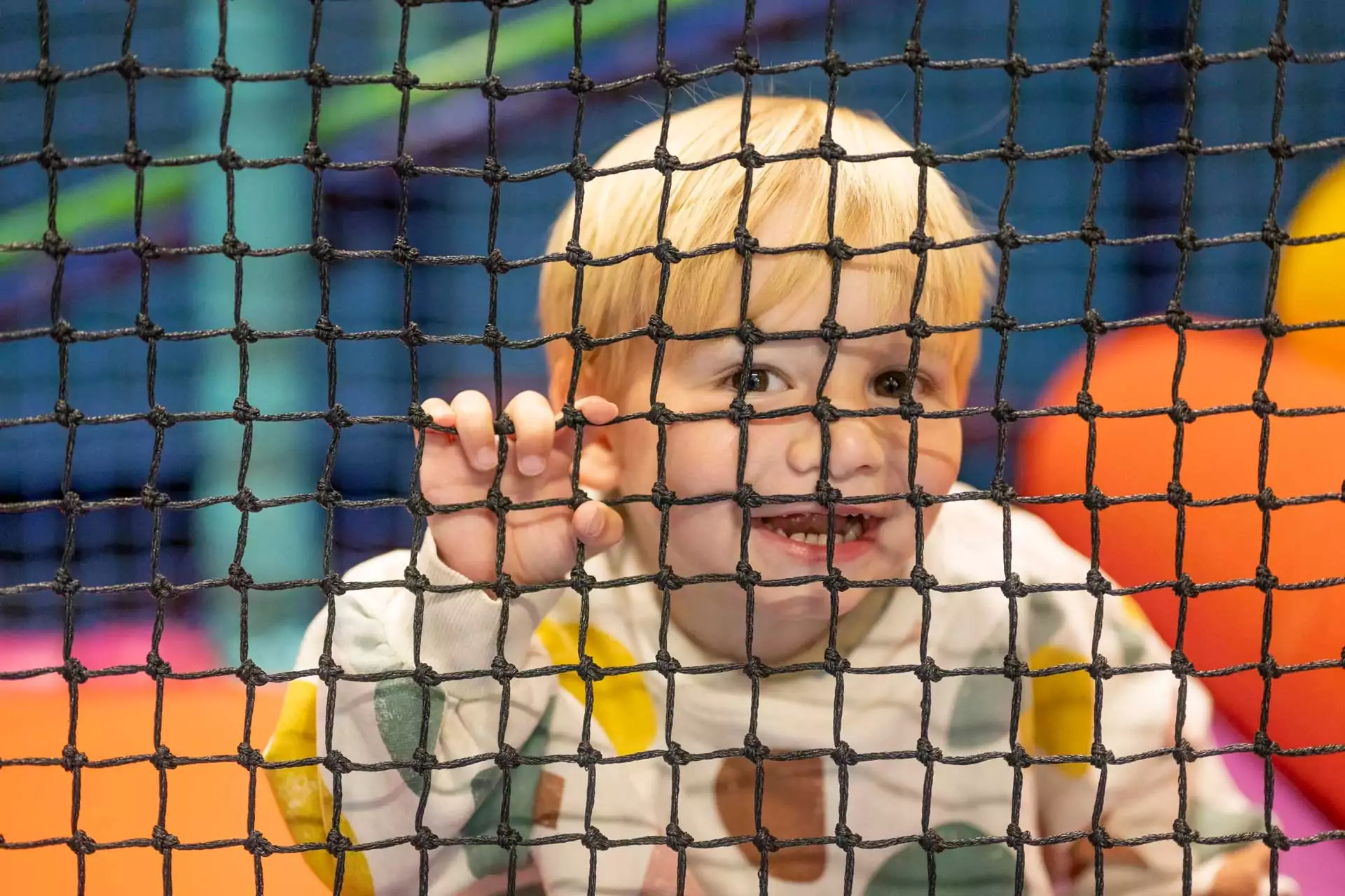 Smiling young child looking through netting inside a colourful indoor soft play area at Meadow Bay Villages