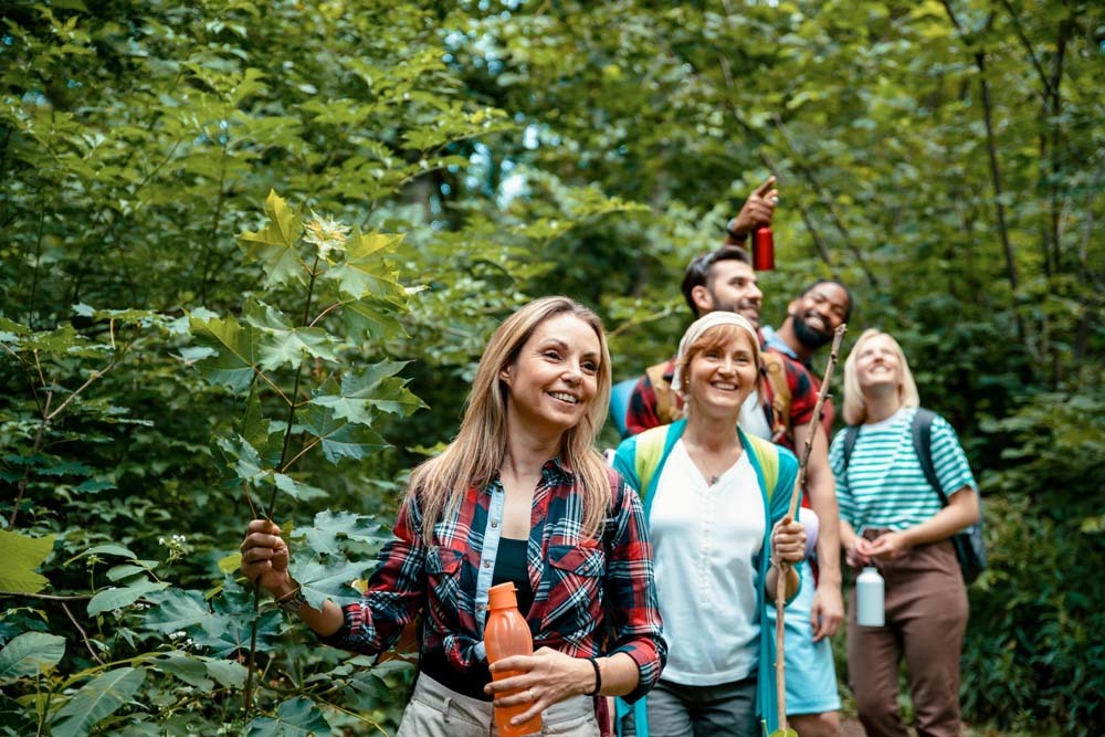 Group of smiling adults enjoying a nature walk through the woodland trails at Billing Aquadrome, part of Meadow Bay Villages, surrounded by lush greenery.