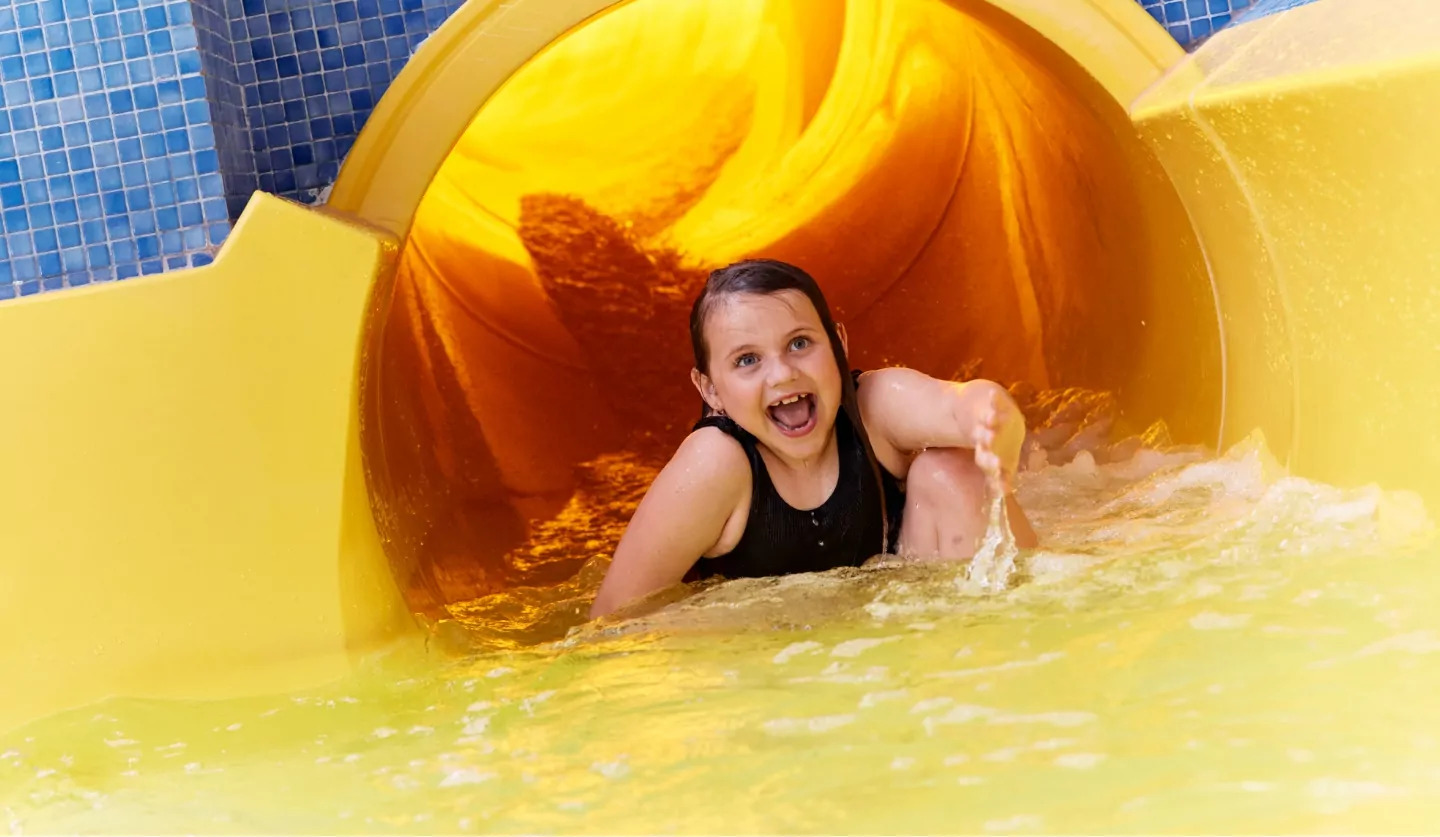 Excited child coming out of a bright yellow indoor waterslide at Billing Aquadrome holiday park