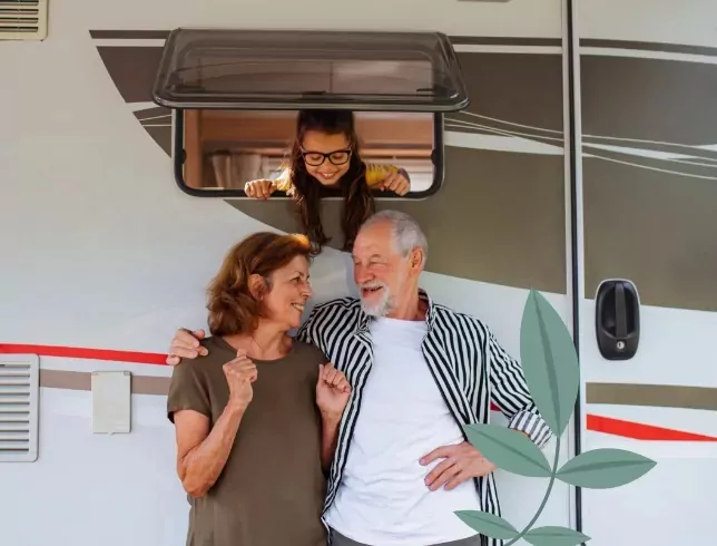 Happy grandparents standing by their caravan with their granddaughter looking out of the window at Billing Aquadrome, Meadow Bay Villages.