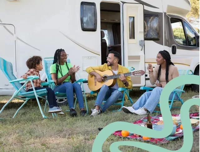 Friends and family relaxing outside a caravan with a picnic and live guitar music at Billing Aquadrome, part of Meadow Bay Villages.