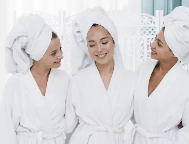 hree smiling women in white robes and towels enjoying a relaxing spa moment together at Billing Aquadrome holiday park
