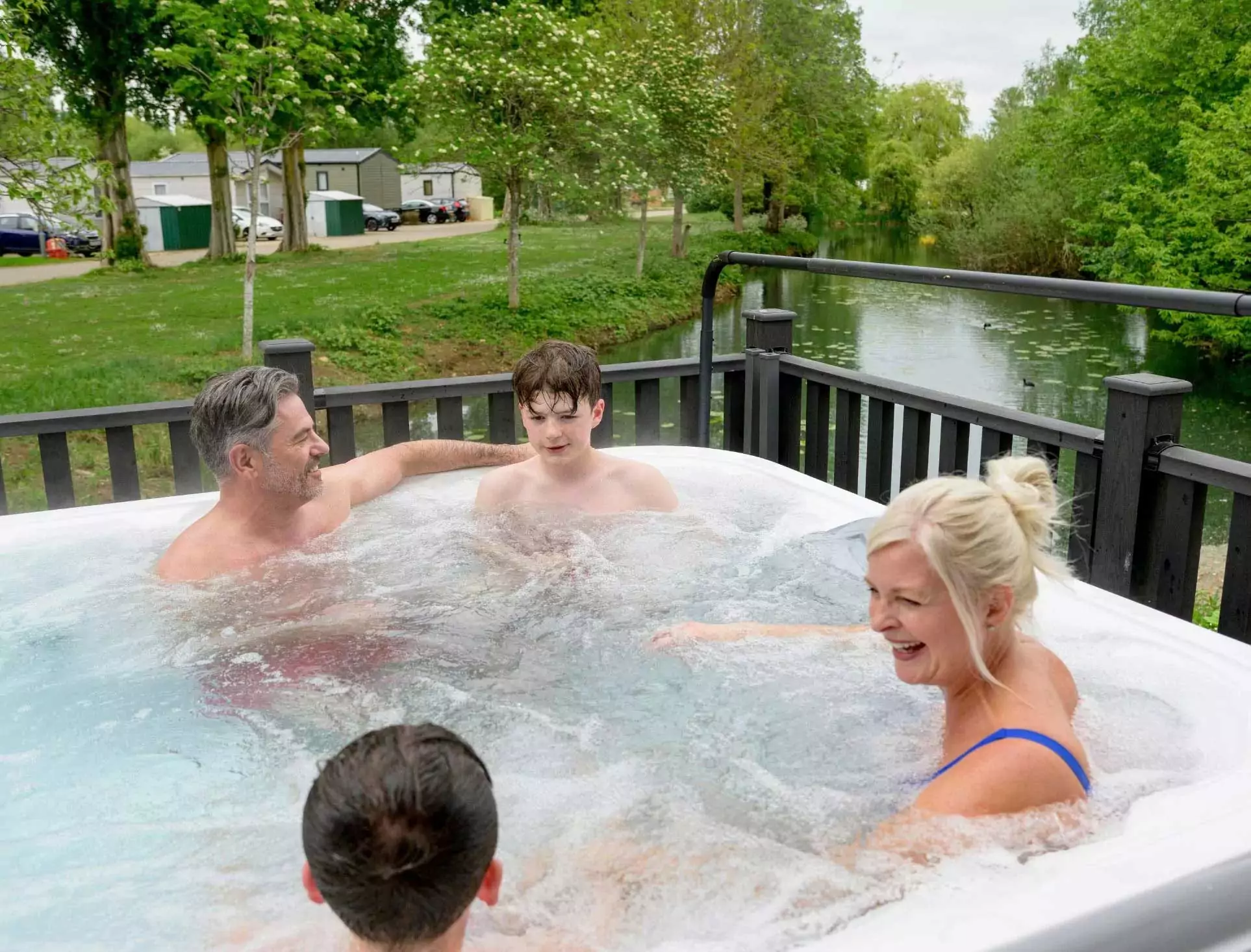 Family enjoying a relaxing soak in a private hot tub on the decking of their lakeside lodge at Billing Aquadrome holiday park