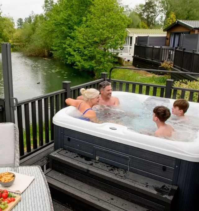 Family relaxing in a private outdoor hot tub at their lodge overlooking the water at Billing Aquadrome holiday park