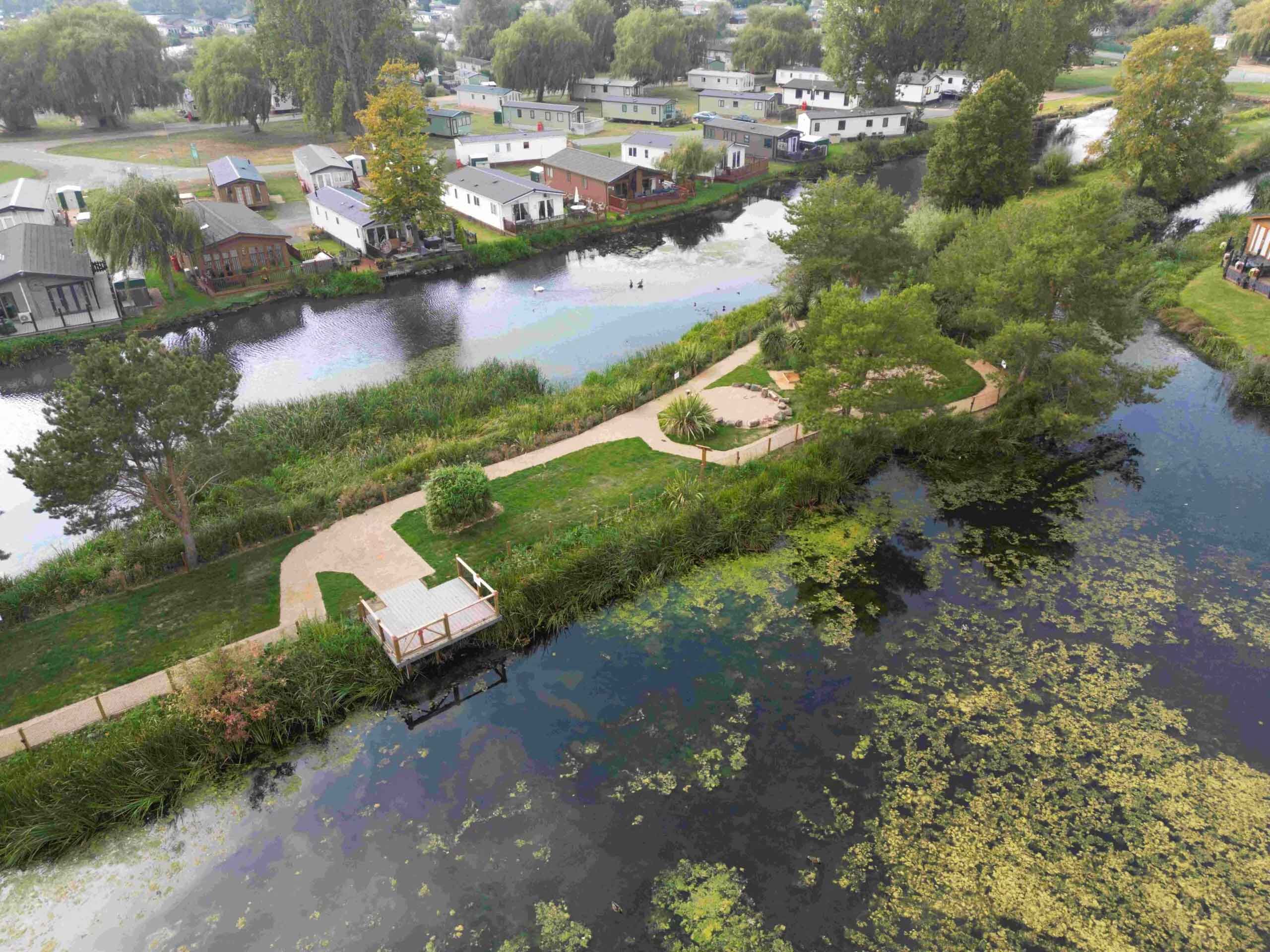 Scenic aerial view of lakeside holiday lodges and peaceful walking paths surrounded by nature at Billing Aquadrome, part of Meadow Bay Villages.