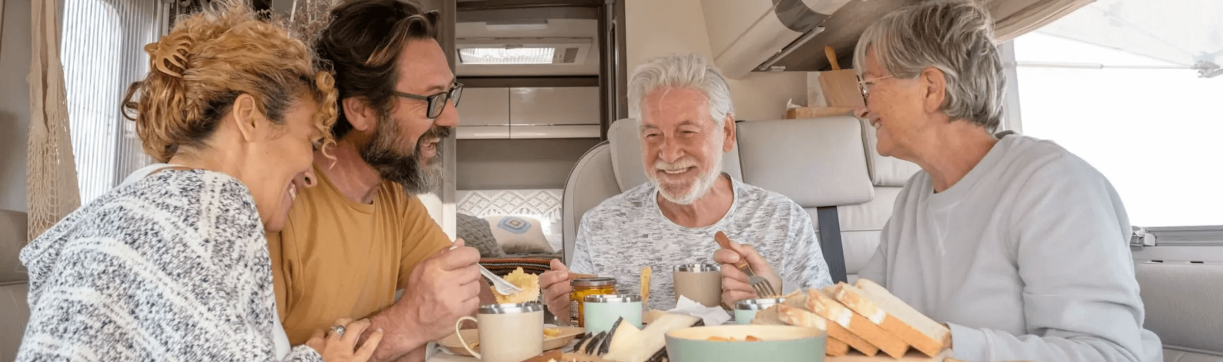 Two couples enjoying breakfast together inside a motorhome at Meadow Bay Villages’ Billing Aquadrome, sharing laughter and good food on a touring holiday
