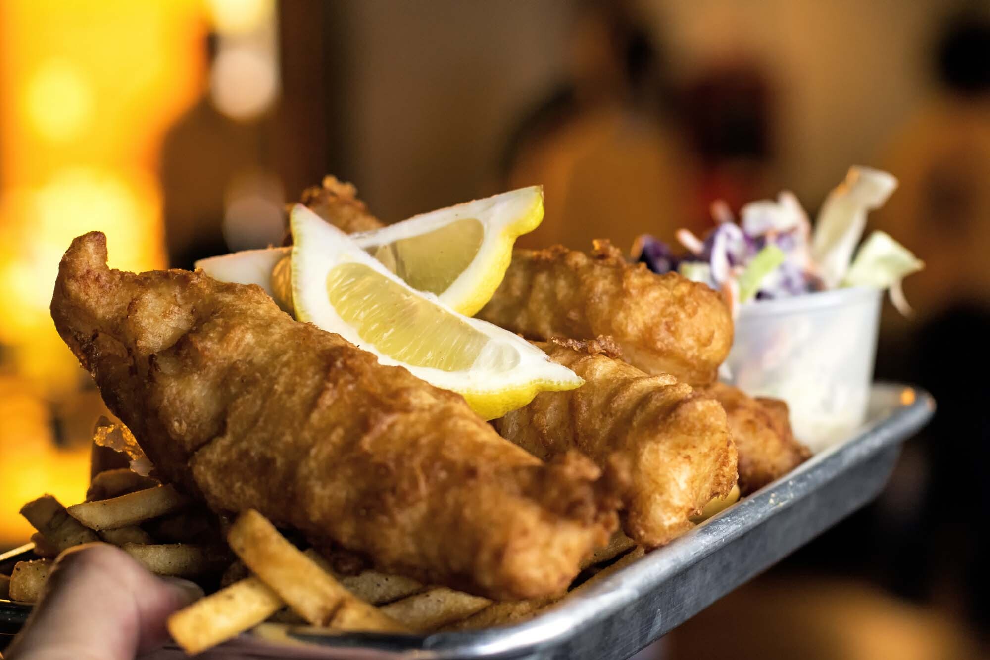 Close-up of a freshly served fish and chips meal with lemon wedges and coleslaw at Meadow Bay Villages – a traditional British holiday favourite.