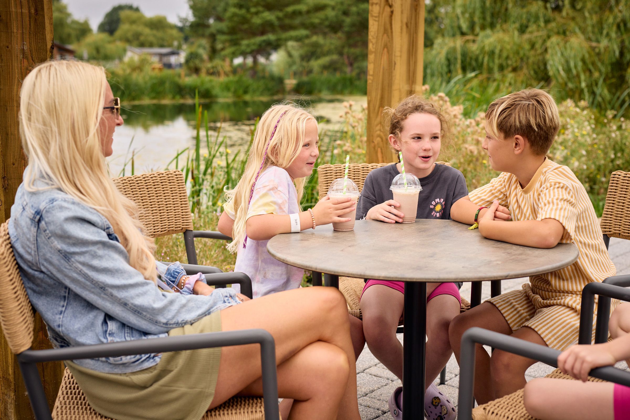 Children enjoying milkshakes with a parent at an outdoor lakeside café at Meadow Bay Villages – relaxed family holiday atmosphere.