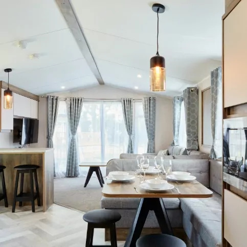 Bright and modern open-plan holiday home interior with dining area, lounge seating, and large windows at Meadow Bay Villages.