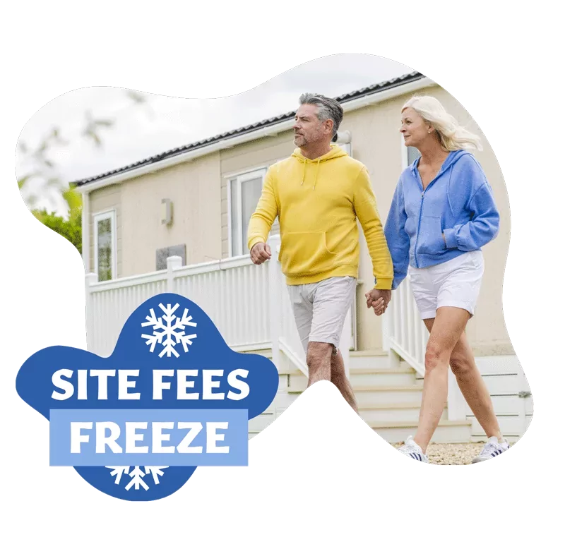 Mature couple walking hand in hand outside a static caravan with a badge promoting site fees freeze at Meadow Bay Villages