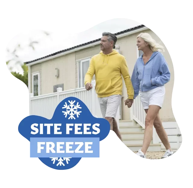 Mature couple walking hand in hand outside a static caravan with a badge promoting site fees freeze at Meadow Bay Villages