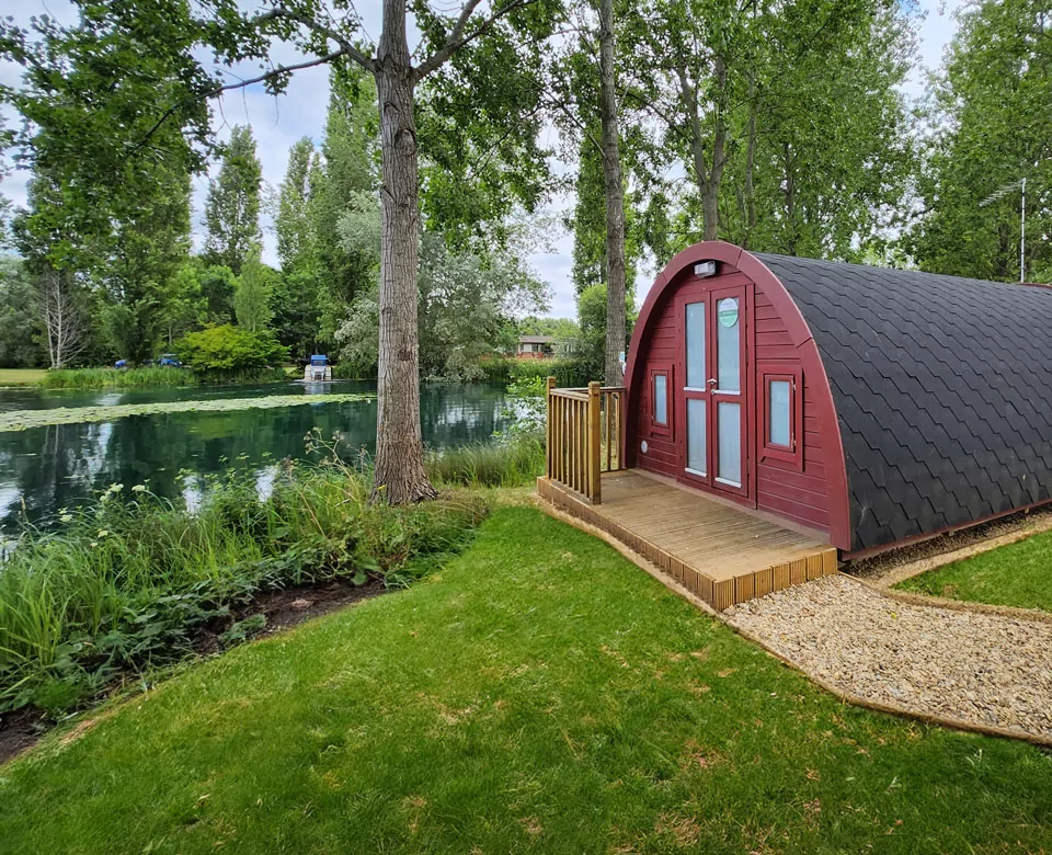Red wooden glamping pod by a serene countryside lake at Billing Aquadrome