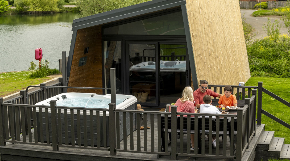 Family enjoying outdoor dining beside a glamping lodge with a private hot tub at Billing Aquadrome.