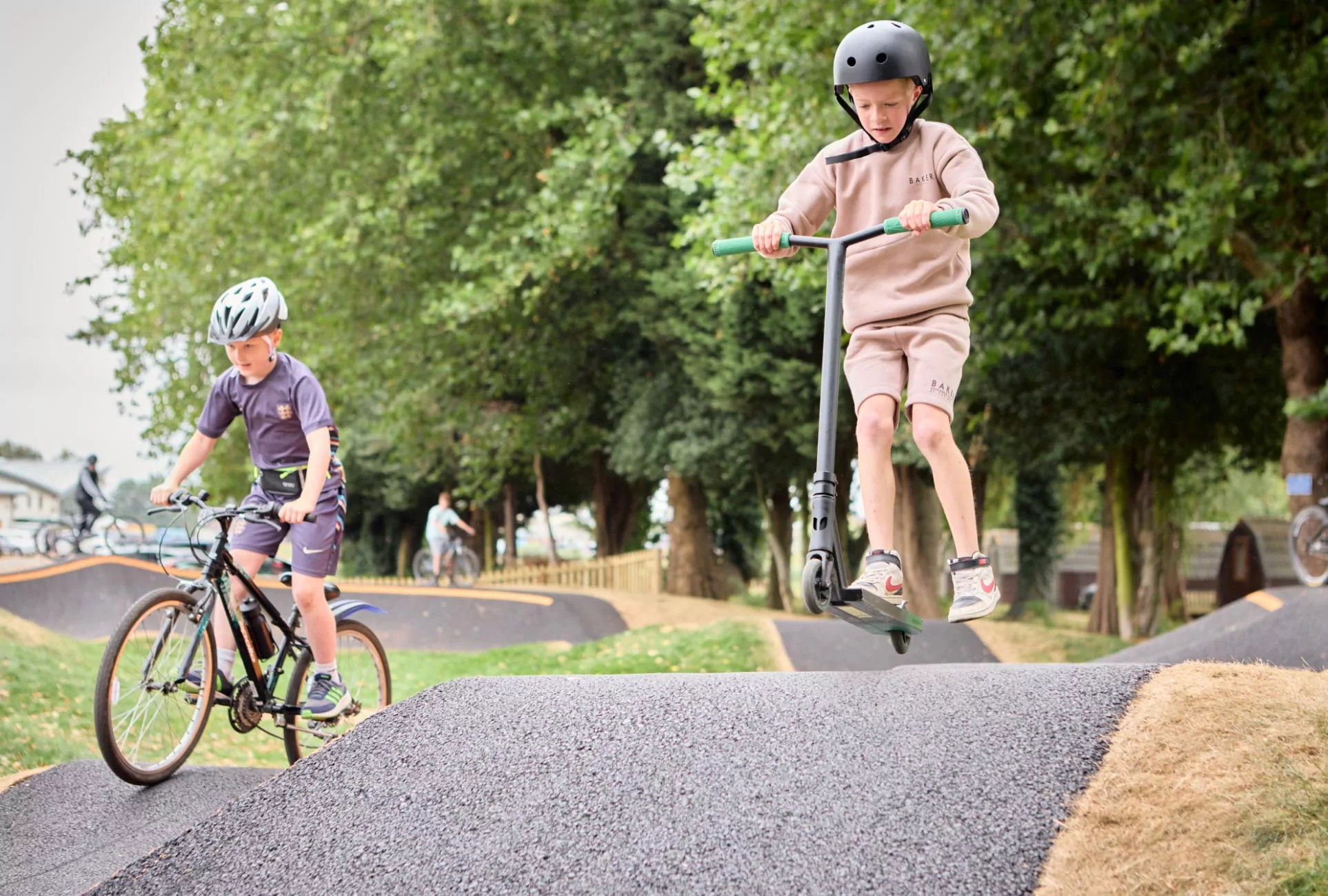 Two young boys performing tricks and riding on the outdoor pump track at Billing Aquadrome