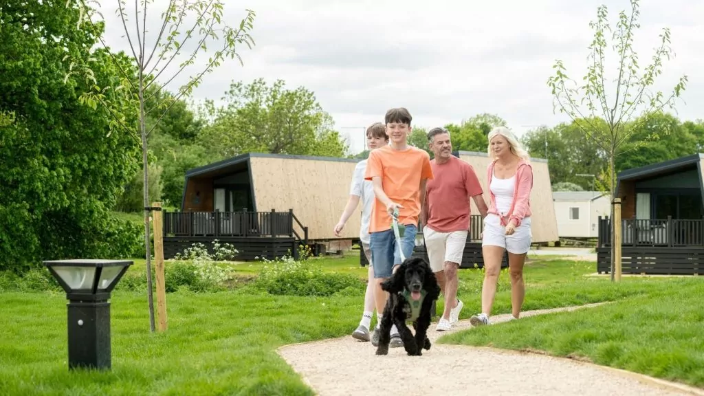 Family walking their dog along a landscaped path between holiday lodges during a relaxing break at Billing Aquadrome