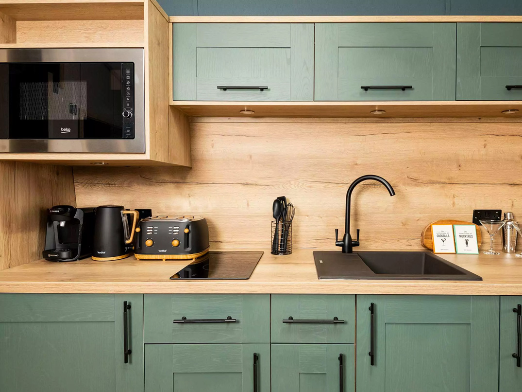 A fully equipped contemporary kitchen featuring sage green cabinetry and integrated appliances at Billing Aquadrome.