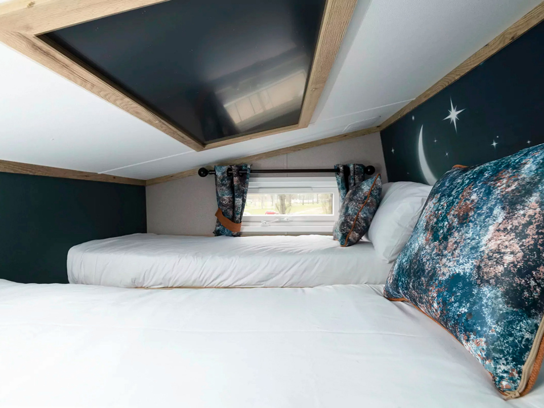 Cozy twin beds in a cleverly designed bedroom with a unique skylight and celestial wall art at Billing Aquadrome.