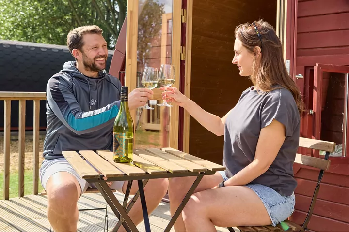 Couple toasting glasses of wine while sitting on the decking of a cosy holiday lodge at Billing Aquadrome