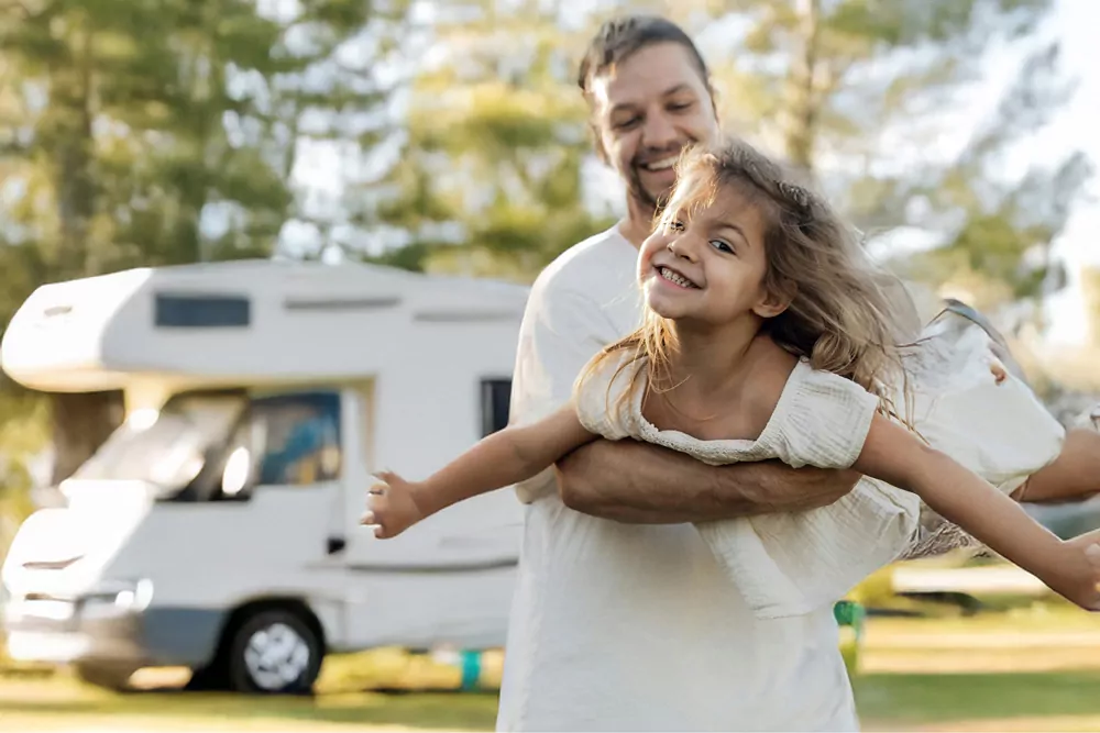 Father lifting his daughter playfully outside a motorhome during a relaxing family holiday at the park, Meadow Bay Villages.