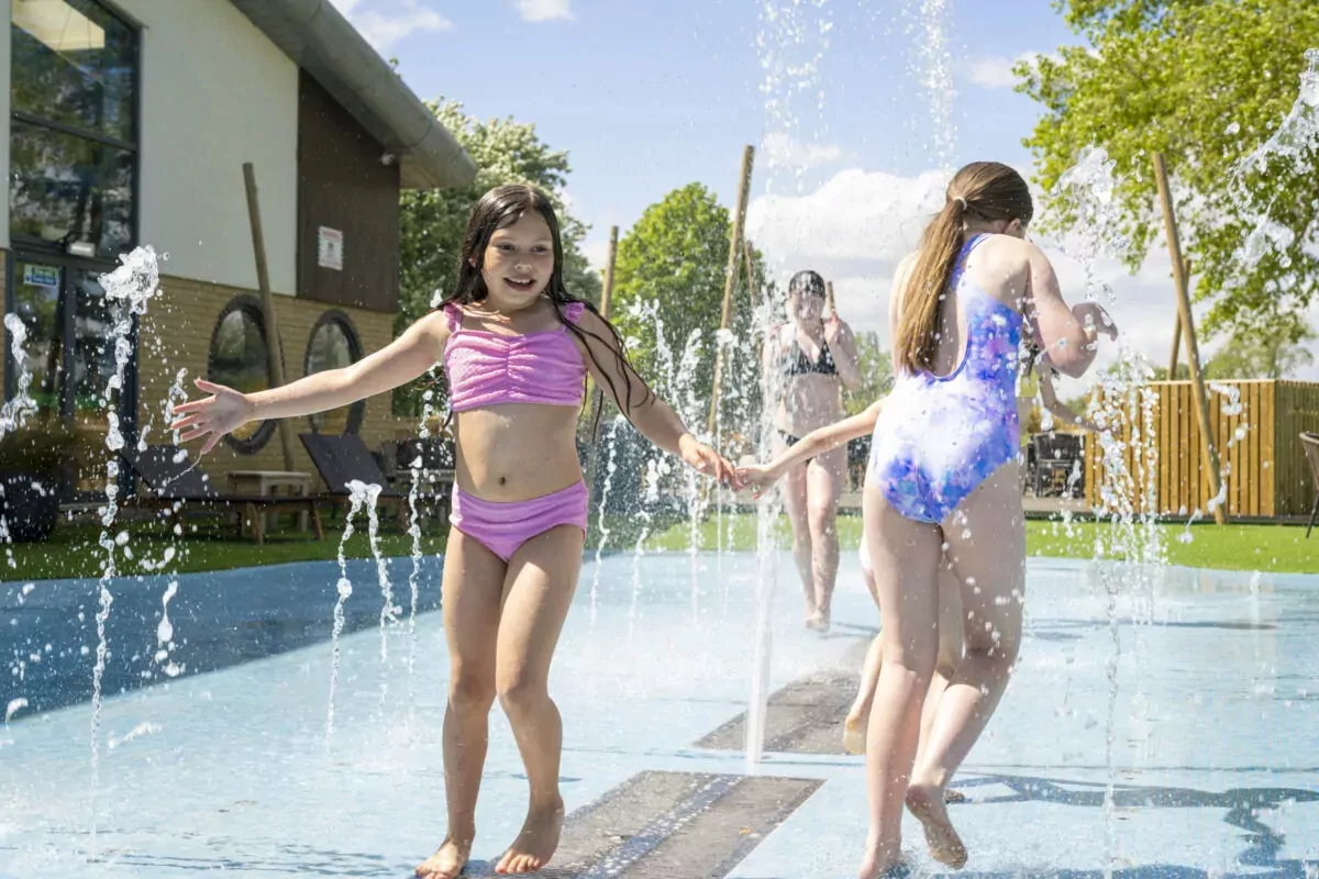 Children playing and running through water jets at the outdoor splash pad on a sunny day at Billing Aquadrome